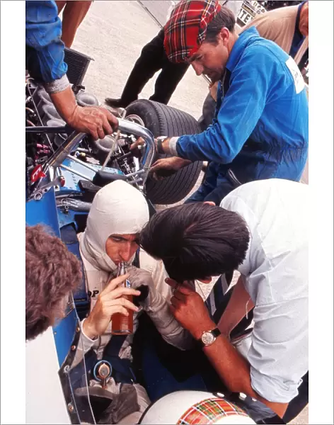 Jackie Stewart has a drink while his mechanics examine the car during practice at the 1969 British Grand Prix