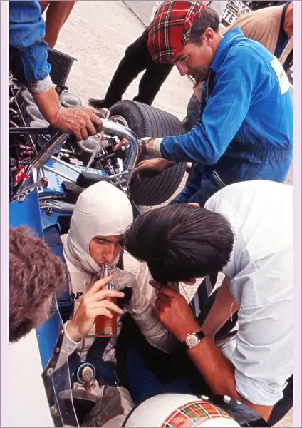 Jackie Stewart has a drink while his mechanics examine the car during practice at the 1969 British Grand Prix