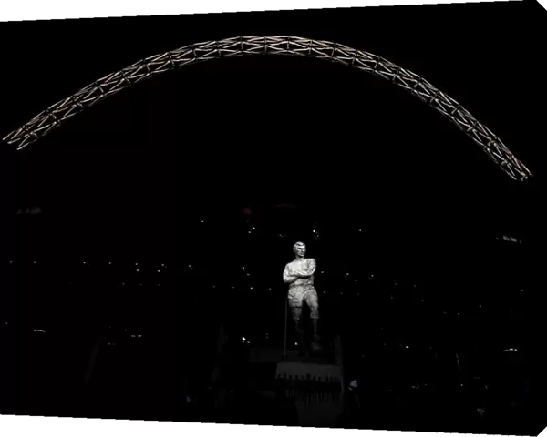 The statue of Bobby Moore stands in front of an illuminated Wembley Stadium