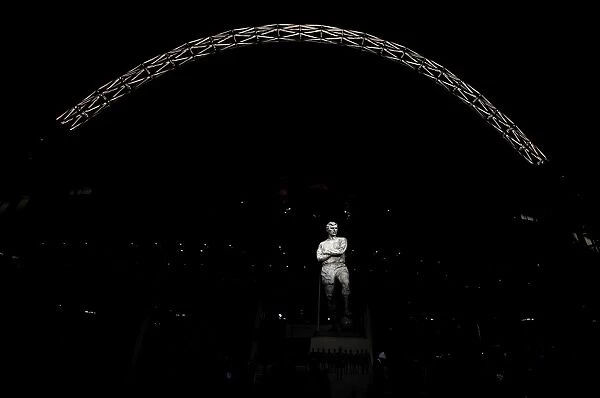 The statue of Bobby Moore stands in front of an illuminated Wembley Stadium