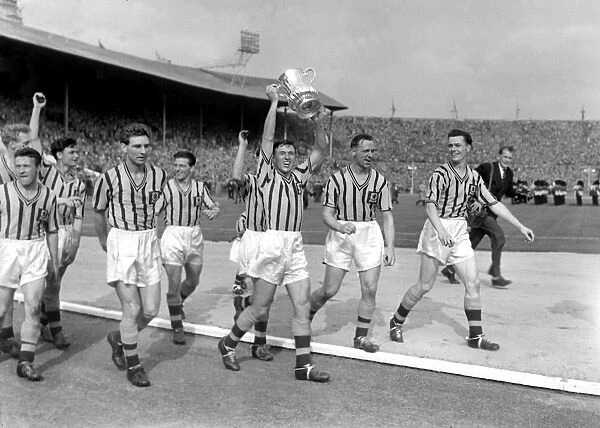 Aston Villa captain Johnny Dixon leads his side on a victory lap with the FA Cup trophy in 1957
