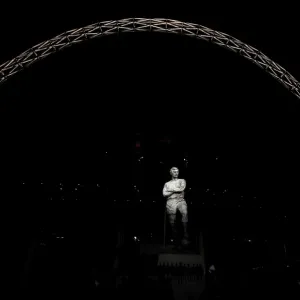 The statue of Bobby Moore stands in front of an illuminated Wembley Stadium