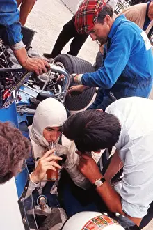 Jackie Stewart has a drink while his mechanics examine the car during practice at the 1969 British Grand Prix